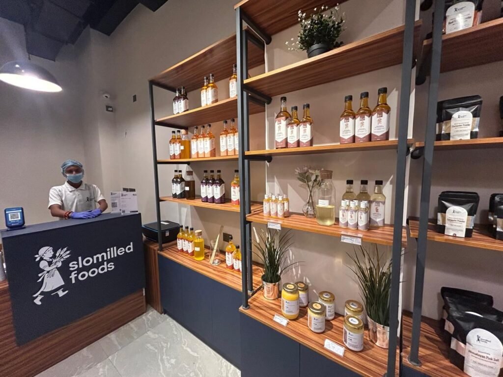 A Slomilled team member at the counter beside shelves of wood-pressed oils and jars of ghee.